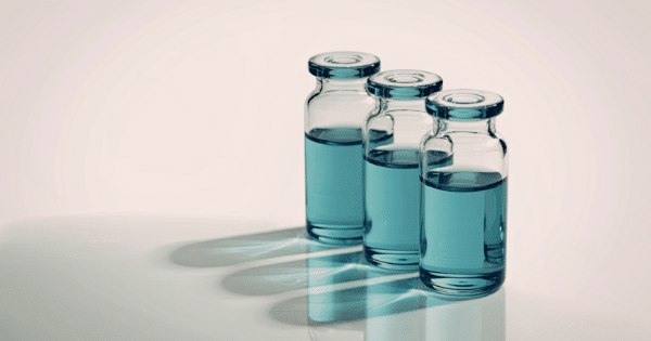 Three small glass vials filled with clear light-blue liquid casting long, sharp shadows on a reflective surface.