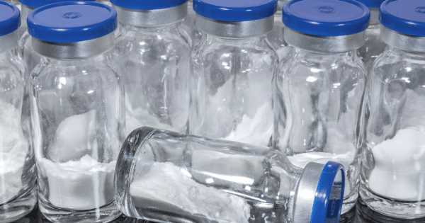 A cluster of glass medical vials containing white lyophilized (freeze-dried) powder sealed with blue caps.