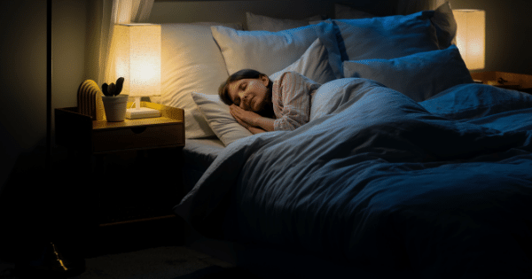 A young woman sleeping peacefully in a cozy bed, illuminated by a warm lamp light on her bedside table.
