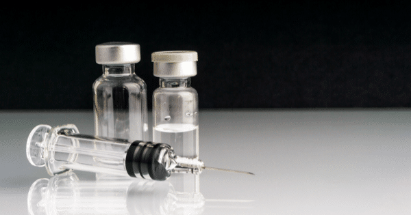 Medical syringe lying in front of two clear glass medicine vials.