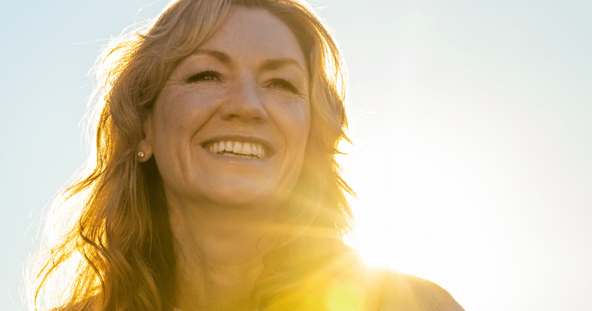 Low-angle portrait of a smiling woman bathed in bright warm sunlight outdoor.