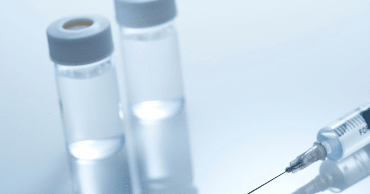 Medical syringe alongside clear glass liquid vials on a reflective surface.