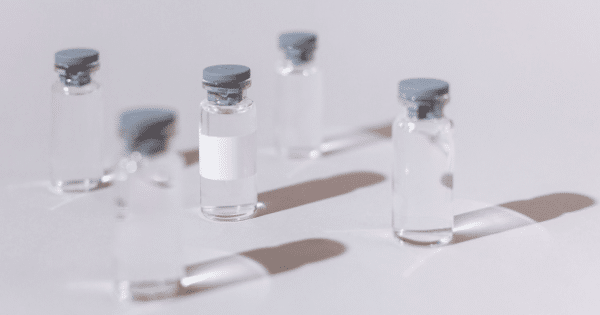 Five small glass medicine vials with rubber stoppers casting soft shadows on a neutral gray surface.