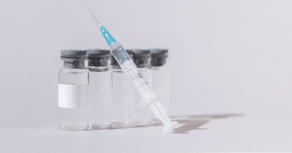 Clear medical syringe resting diagonally across a row of small glass liquid vials.