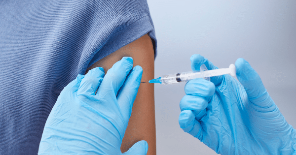 Healthcare professional in blue nitrile gloves administering an injection into a patient's upper arm with a syringe.