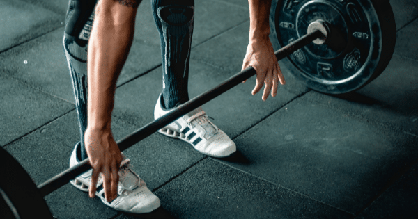 Close-up of an athlete's hands gripping a weighted barbell off the rubber floor during a deadlift exercise.