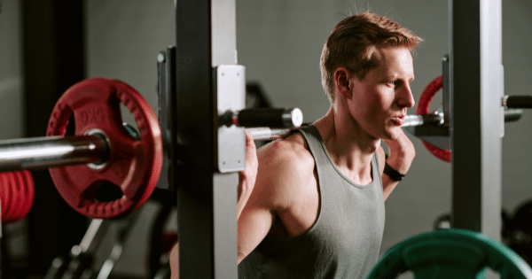 Man performing a barbell back squat inside a power rack at a gym.