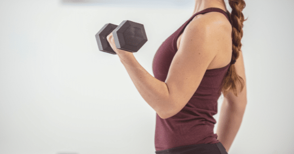 A side profile close-up showing a woman with a braided ponytail wearing a maroon tank top while executing a bicep curl with a single black dumbbell.