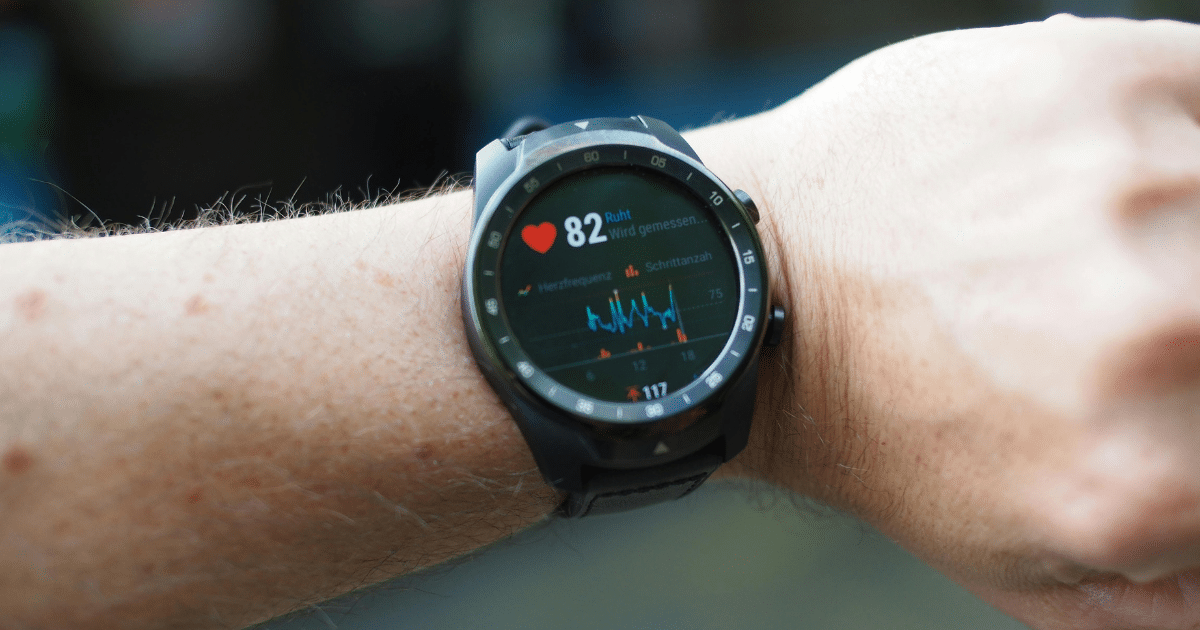 A close-up shot of a person's wrist wearing a black smartwatch that displays a heart rate monitor reading "82" alongside a real-time line graph