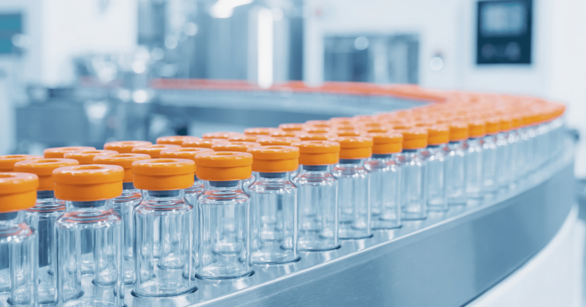 Rows of empty glass medical vials with orange caps moving along an automated factory conveyor belt.