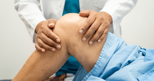 A close-up view of a doctor or physical therapist performing a knee examination on a patient lying down in a medical setting.