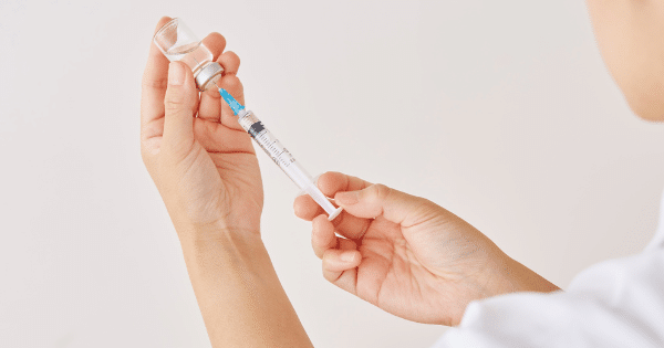 A close-up shot of hands holding a clear medication vial while filling a syringe with a needle.