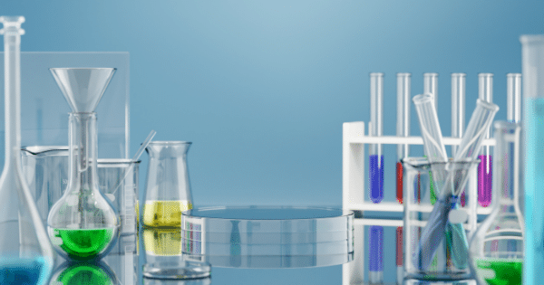 Laboratory setup with glass prove beakers, flasks containing colored liquids, and test tube racks around a central glass display stand.