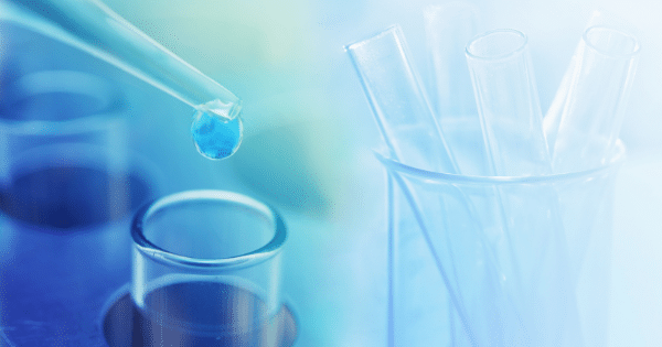 A laboratory scene featuring a glass pipette releasing a blue liquid drop into a test tube alongside a beaker filled with test tubes.