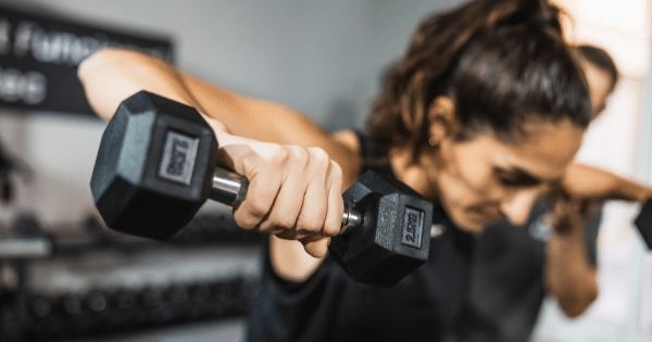 A close-up focus on a woman holding a dumbbell while performing a upper-body resistance exercise.