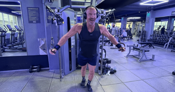 A smiling, athletic man wearing headphones while performing cable chest crossovers on a gym machine.