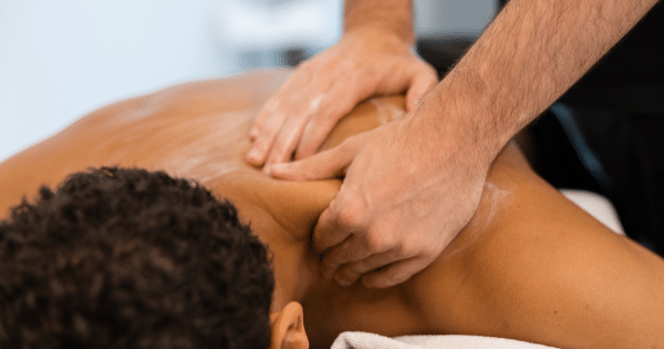 A physical therapist or massage therapist applying pressure to a client's upper back and shoulder area.