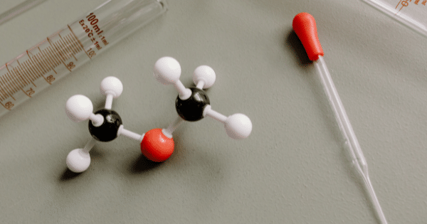 High-angle shot of a molecular model, graduated cylinder, and glass pipette on a plain surface.