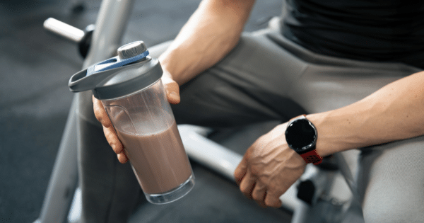 Close-up of a person in fitness wear holding a protein shaker bottle while seated in a gym.
