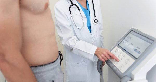 A healthcare professional in a white coat operating a body composition analysis machine for a shirtless male patient in a clinical setting