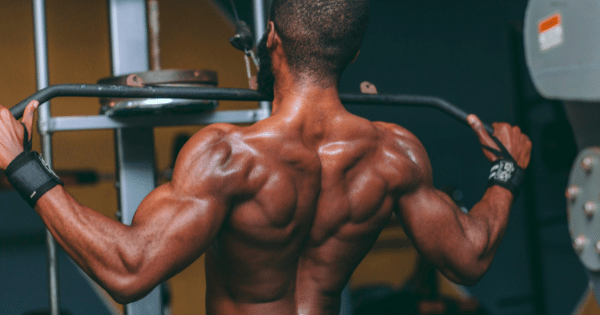 Rear view of a muscular man performing a lat pulldown exercise on a cable machine in a gym setting.