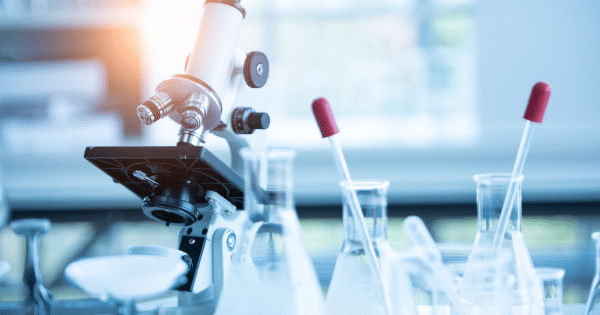 A laboratory setup featuring a medical microscope alongside clear glass flasks with red-capped droppers.