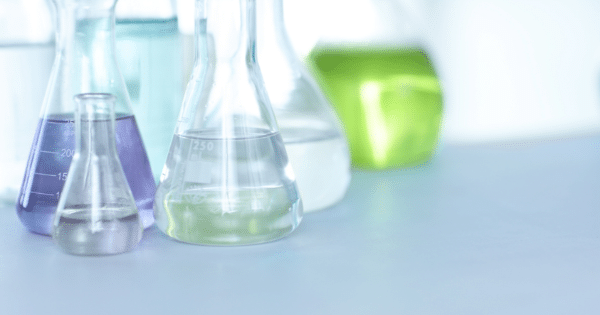 A collection of laboratory Erlenmeyer flasks containing various colored and clear liquids on a white surface.